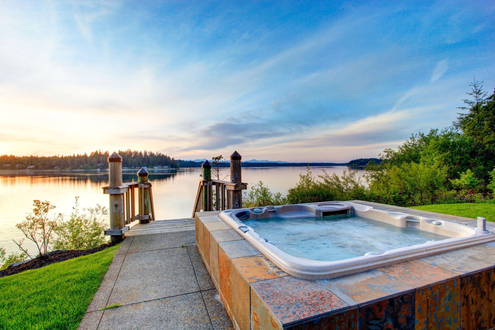 Hot tub on a patio overlooking a calm lake at sunset.