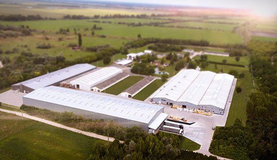 Aerial view of an industrial complex with several white-roofed buildings surrounded by green fields and trees.