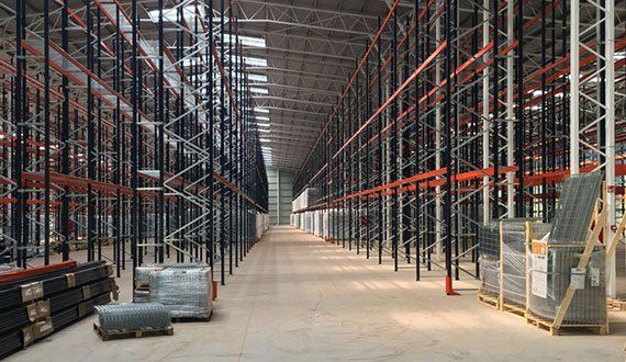 Empty industrial warehouse interior with tall metal shelving and concrete floor.