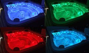 Four hot tubs illuminated with blue, green, red, and purple lights in a dark setting.