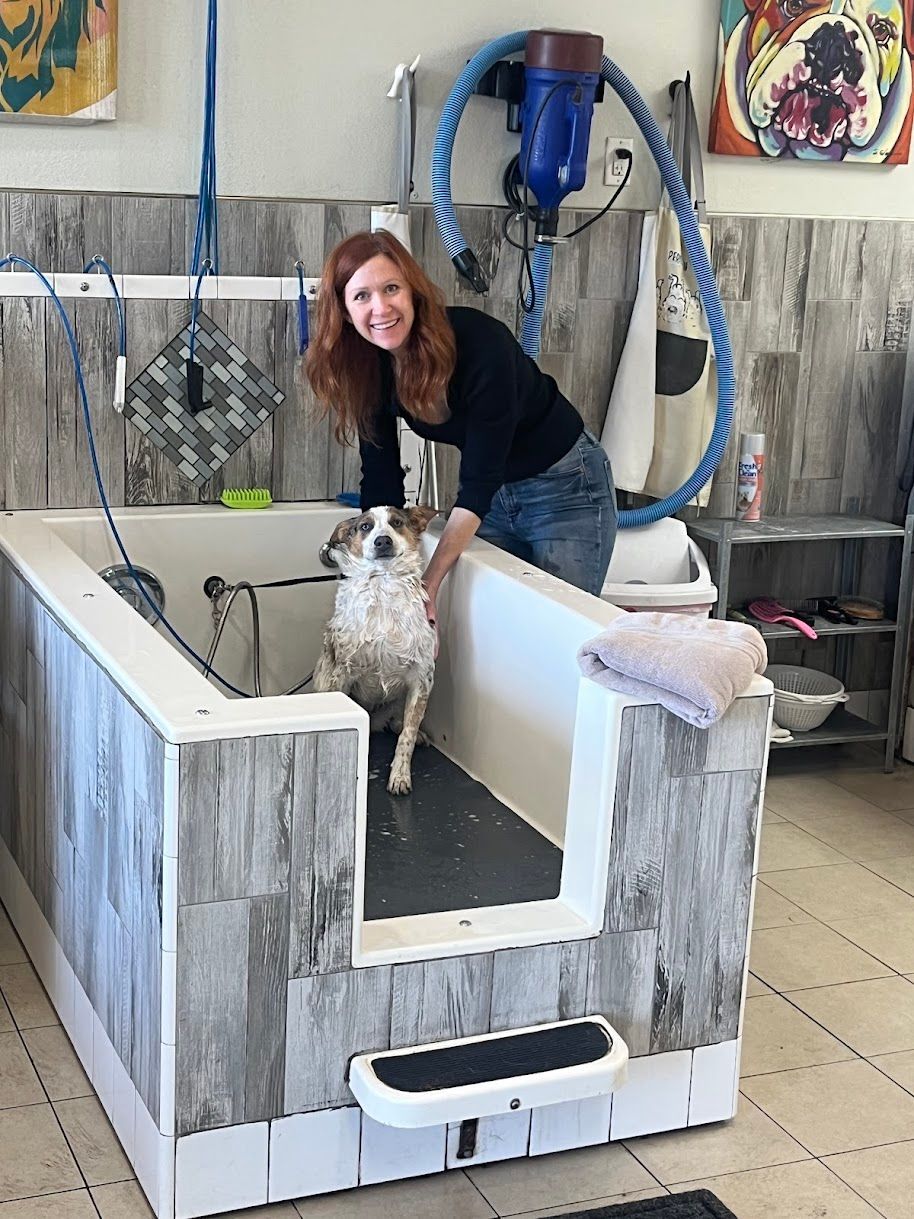 A woman is standing next to a dog in a bathtub.