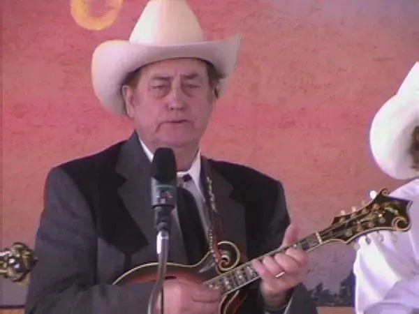 A man in a cowboy hat is playing a guitar in front of a microphone