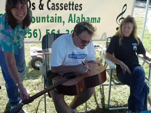 A man playing a guitar in front of a sign that says os & cassettes
