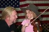 A man and a little girl are playing a violin in front of an american flag.