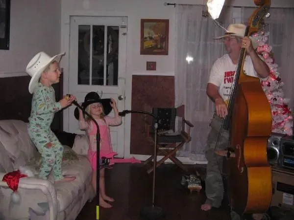 A man playing a double bass in a living room with two children