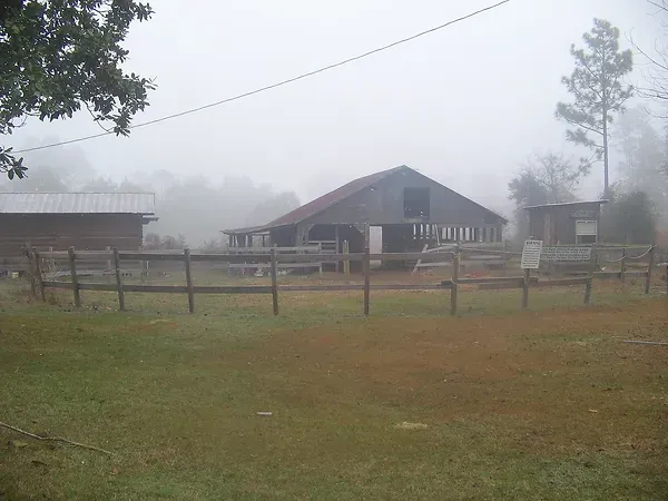 A barn is surrounded by a wooden fence on a foggy day.