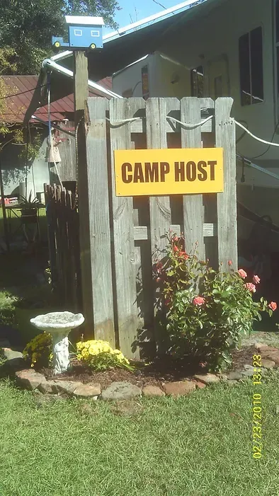 A yellow sign on a wooden fence says camp host