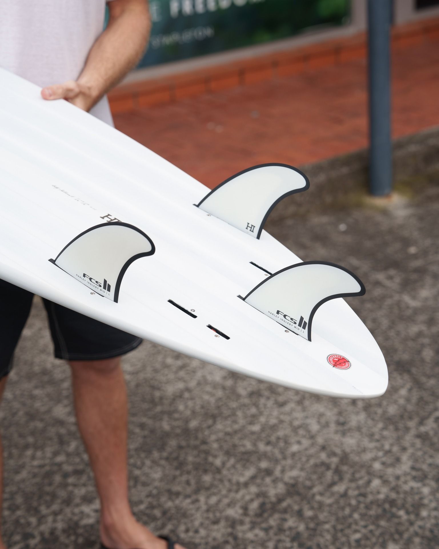 A Man is Holding a White Surfboard With Three Fins on It — Slimes Boardstore in Erina, NSW