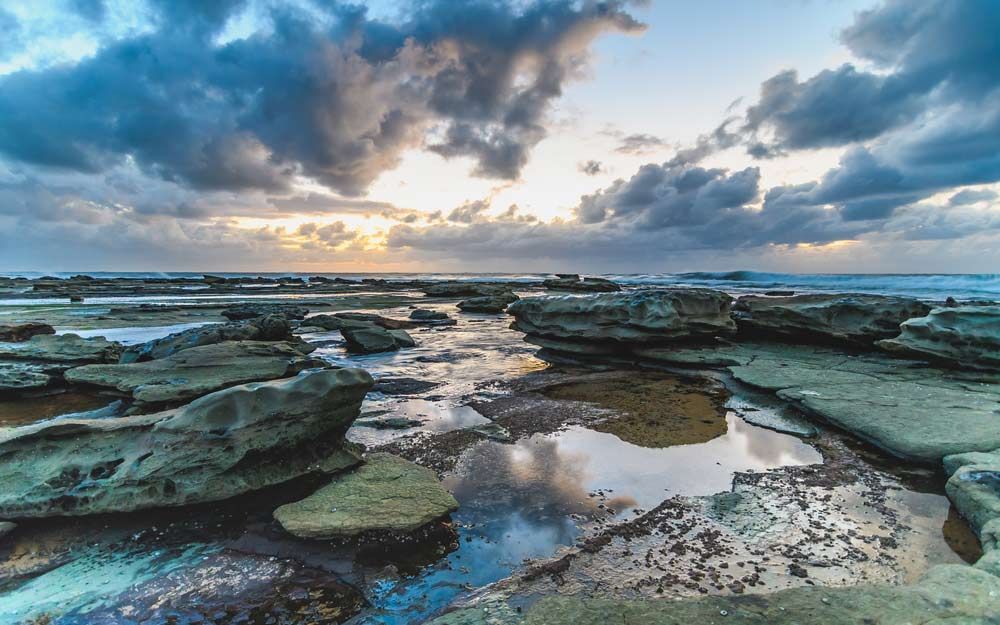 A Sunset Over a Rocky Beach With a Cloudy Sky — Slimes Boardstore in Lisarow, NSW