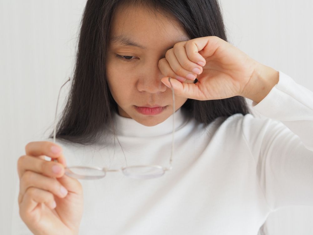 A Woman Is Rubbing Her Eyes While Holding a Pair of Glasses — John Williams Optometrist in Grafton, NSW