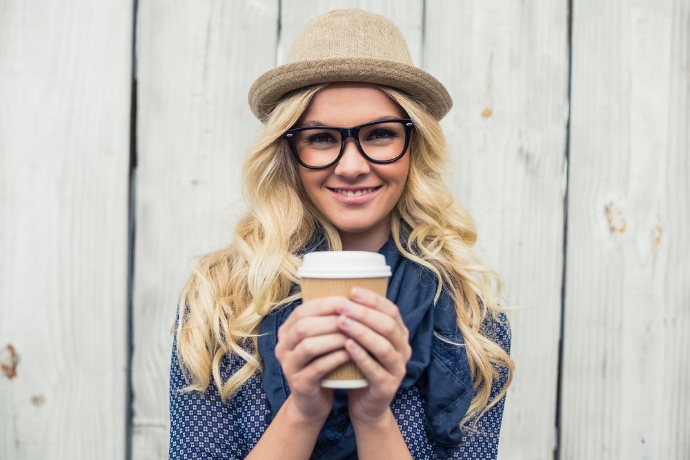 A Woman Wearing Glasses and A Hat Is Holding a Cup of Coffee — John Williams Optometrist in Grafton, NSW