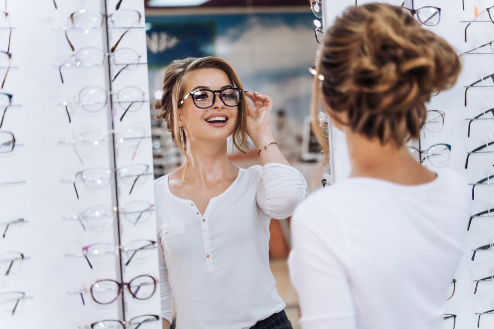 A Woman Is Trying on Glasses in Front of A Mirror — John Williams Optometrist in Grafton, NSW