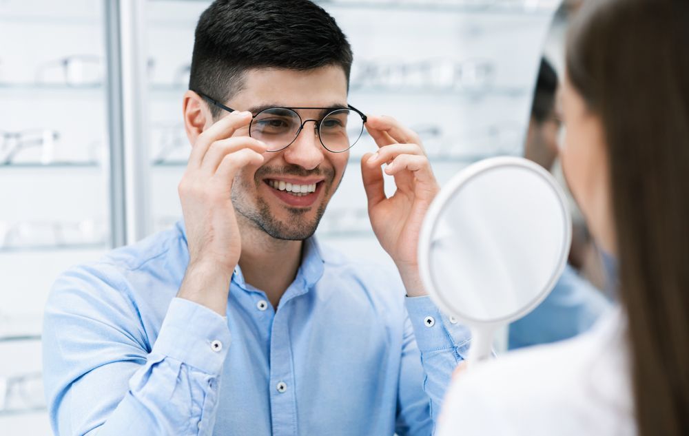 A Man Is Trying on Glasses in Front of A Mirror — John Williams Optometrist in Grafton, NSW 