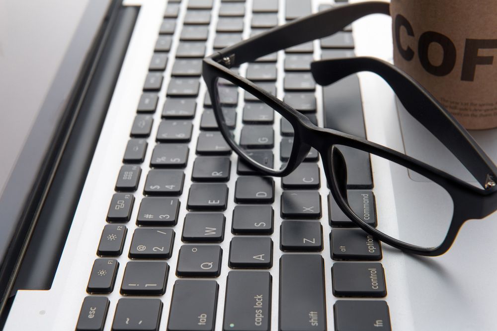 A Pair of Glasses Rests on A Laptop Keyboard Next to A Cup of Coffee — John Williams Optometrist in Grafton, NSW