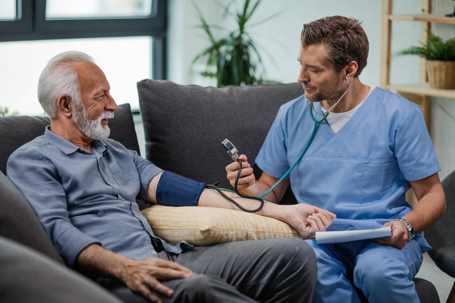 Healthcare worker taking a man's blood pressure on a couch in a living room