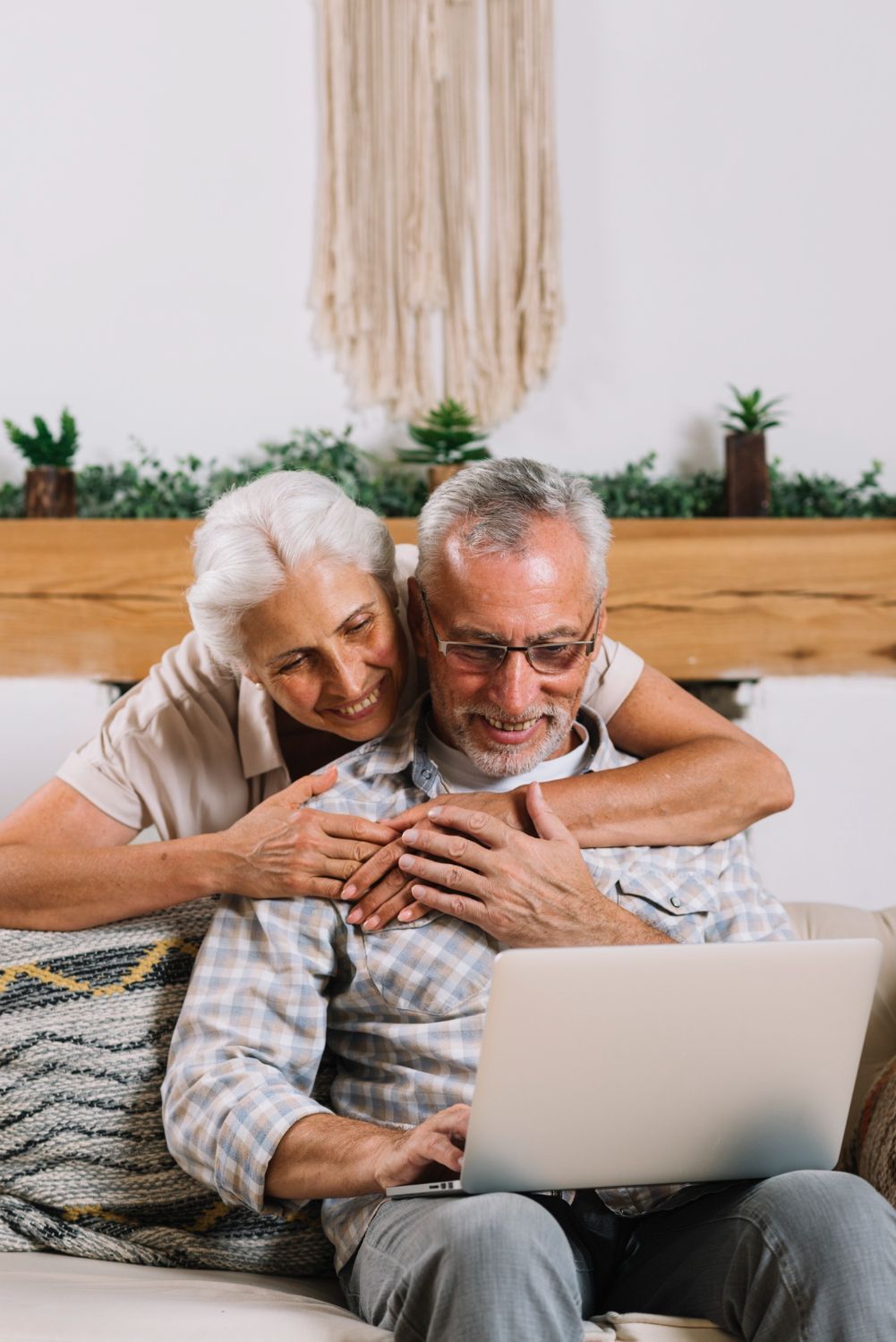 Older couple embracing while using a laptop on a couch in a cozy room