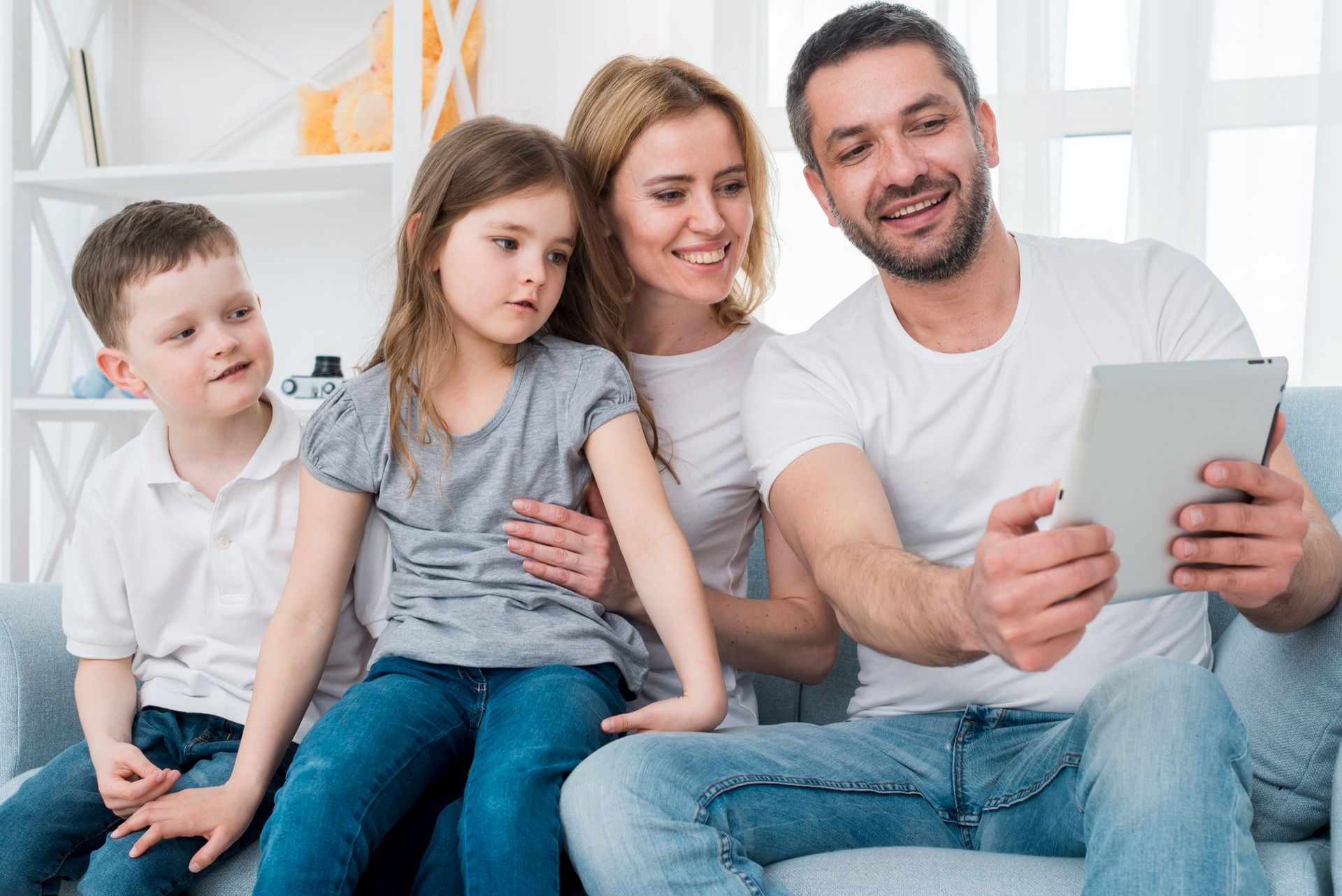Family sitting on a couch, smiling and looking at a tablet together