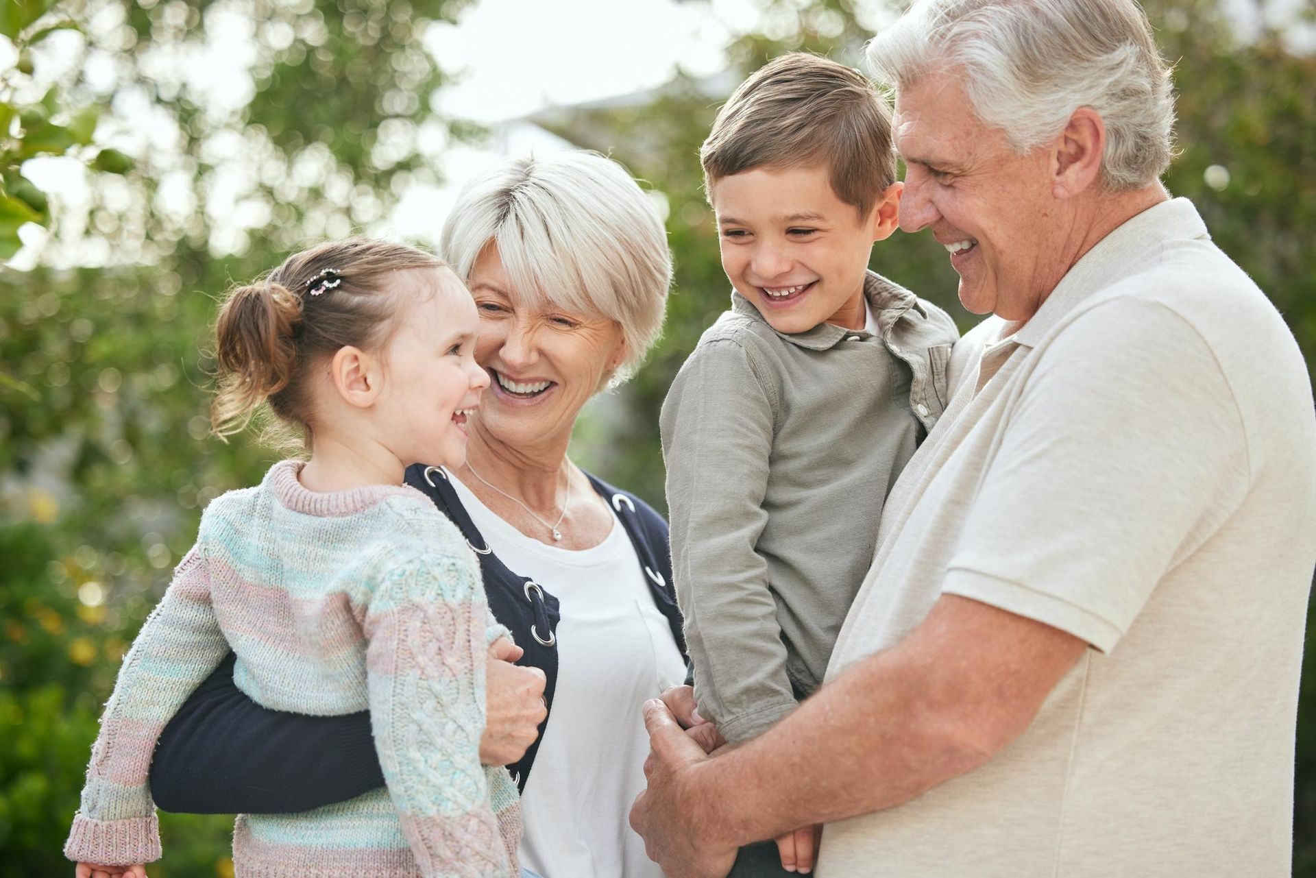 Four people smiling and embracing outdoors in a sunny park.
