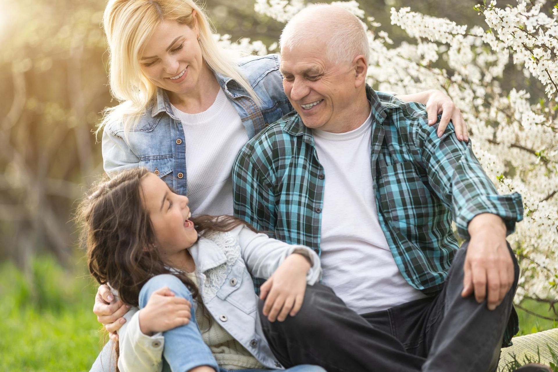 Three people smiling together in a sunlit park, with flowers in the background
