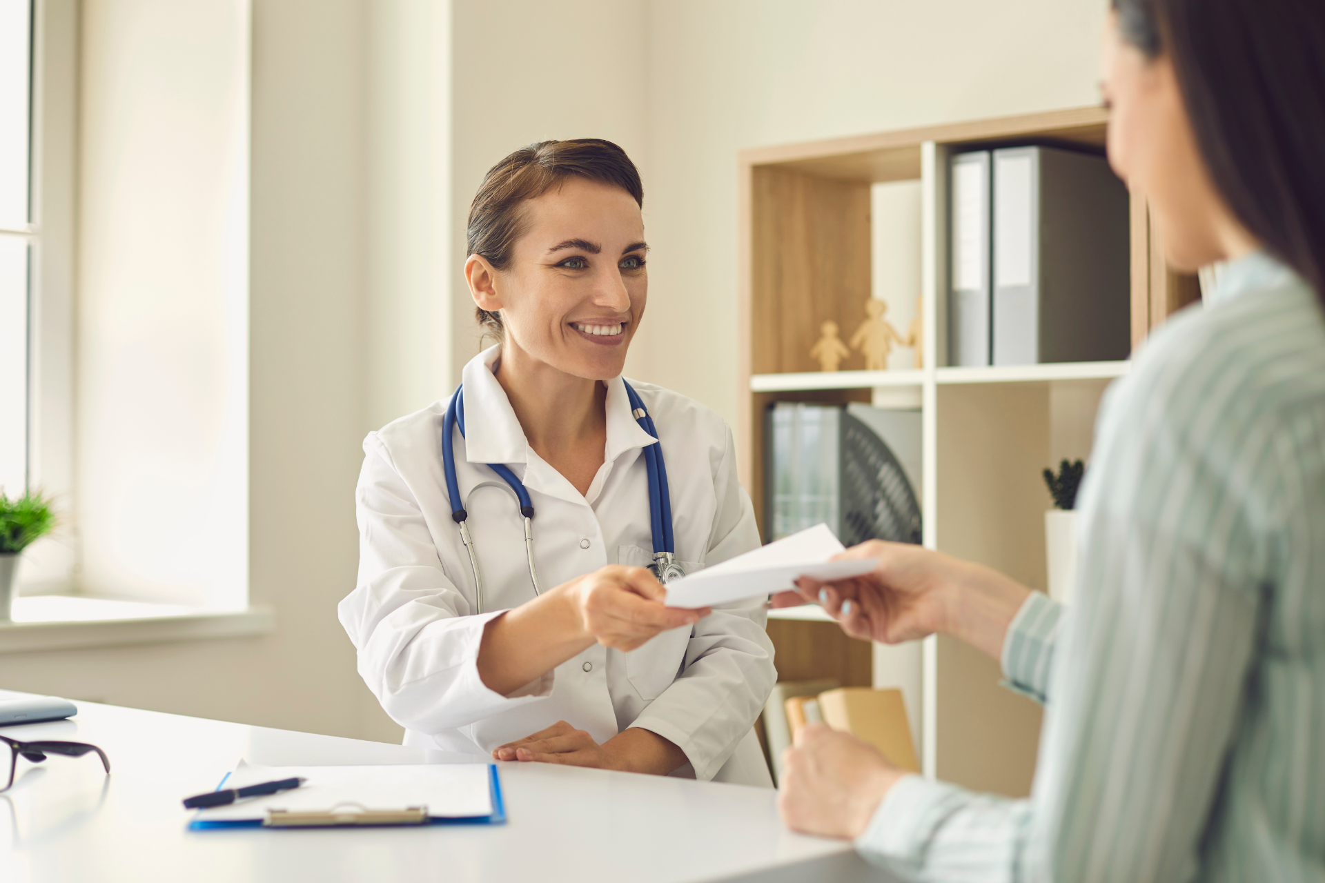 Doctor smiling and handing paperwork to a visitor in a bright office