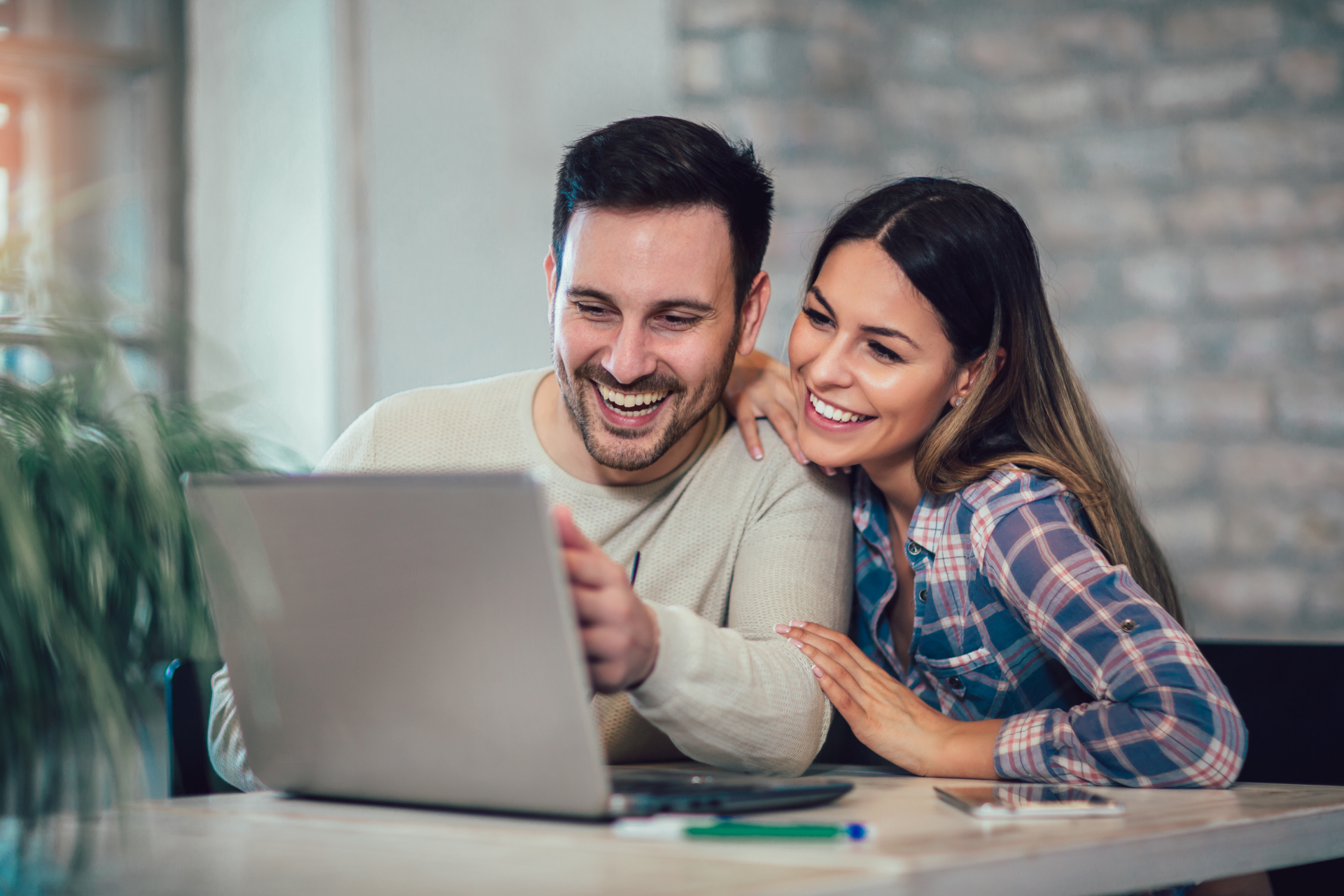 Two people smiling and looking at a laptop on a table in a bright room
