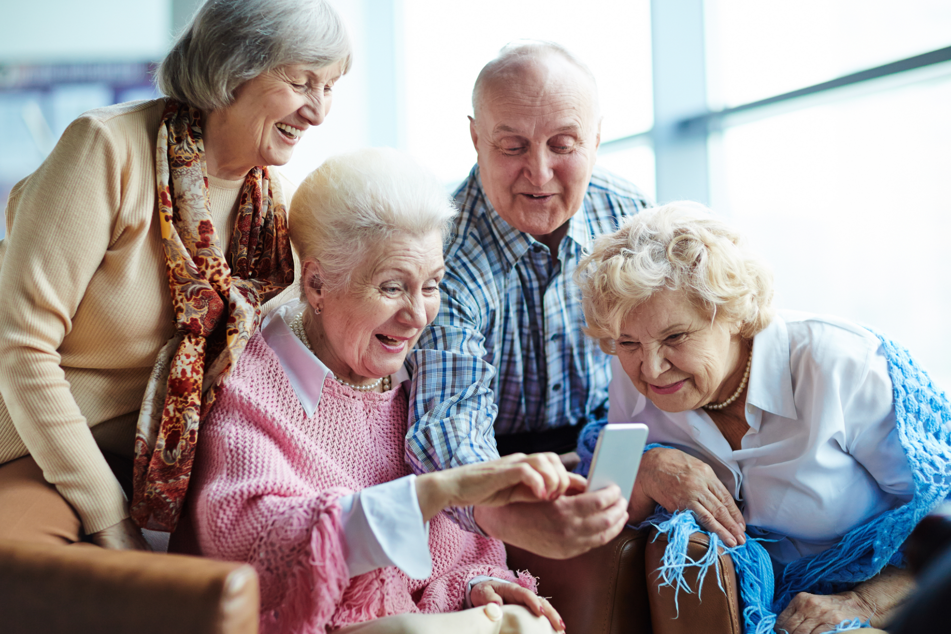 Four seniors smiling and looking at a smartphone together on a couch
