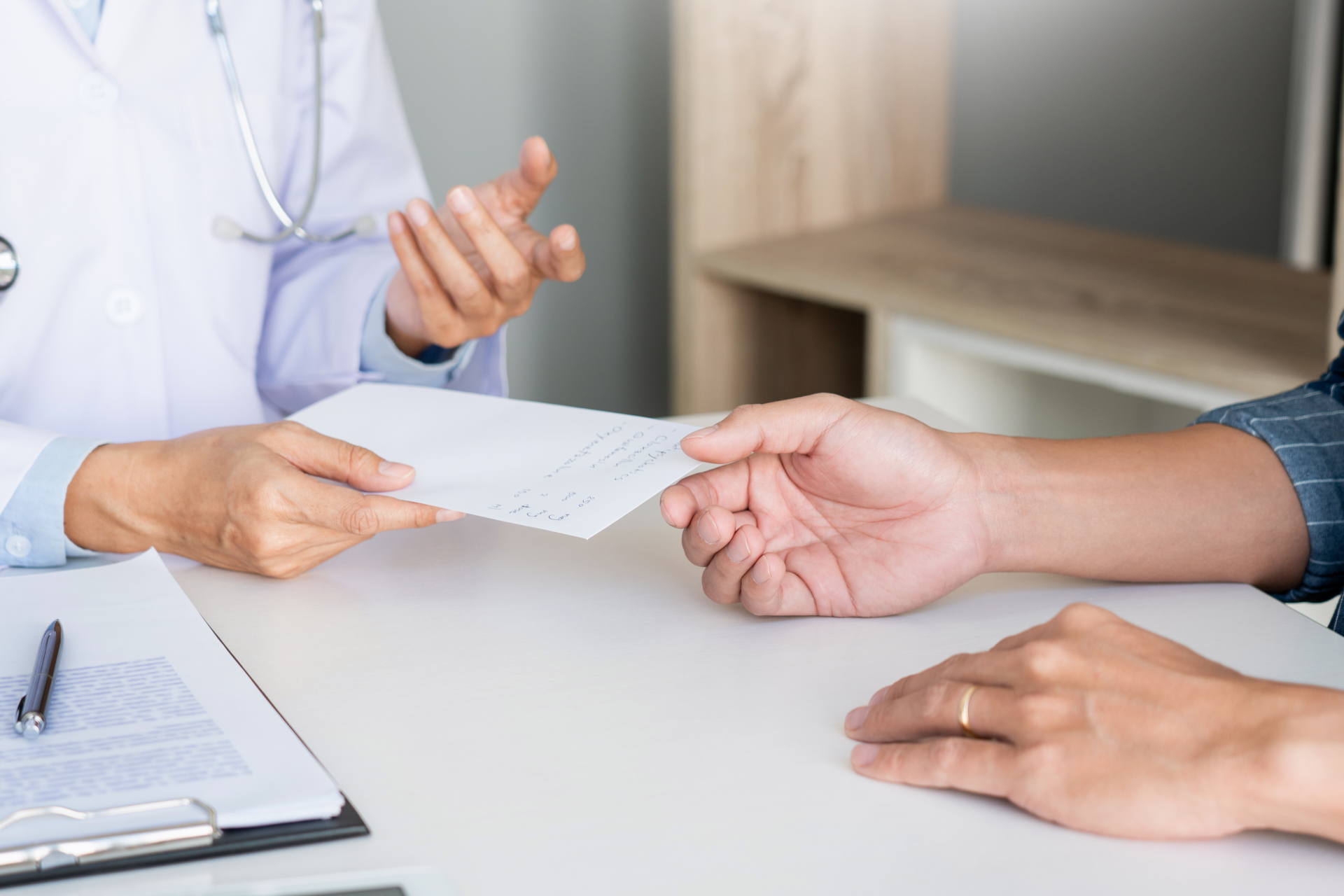Doctor handing a document to a patient across a desk during a consultation