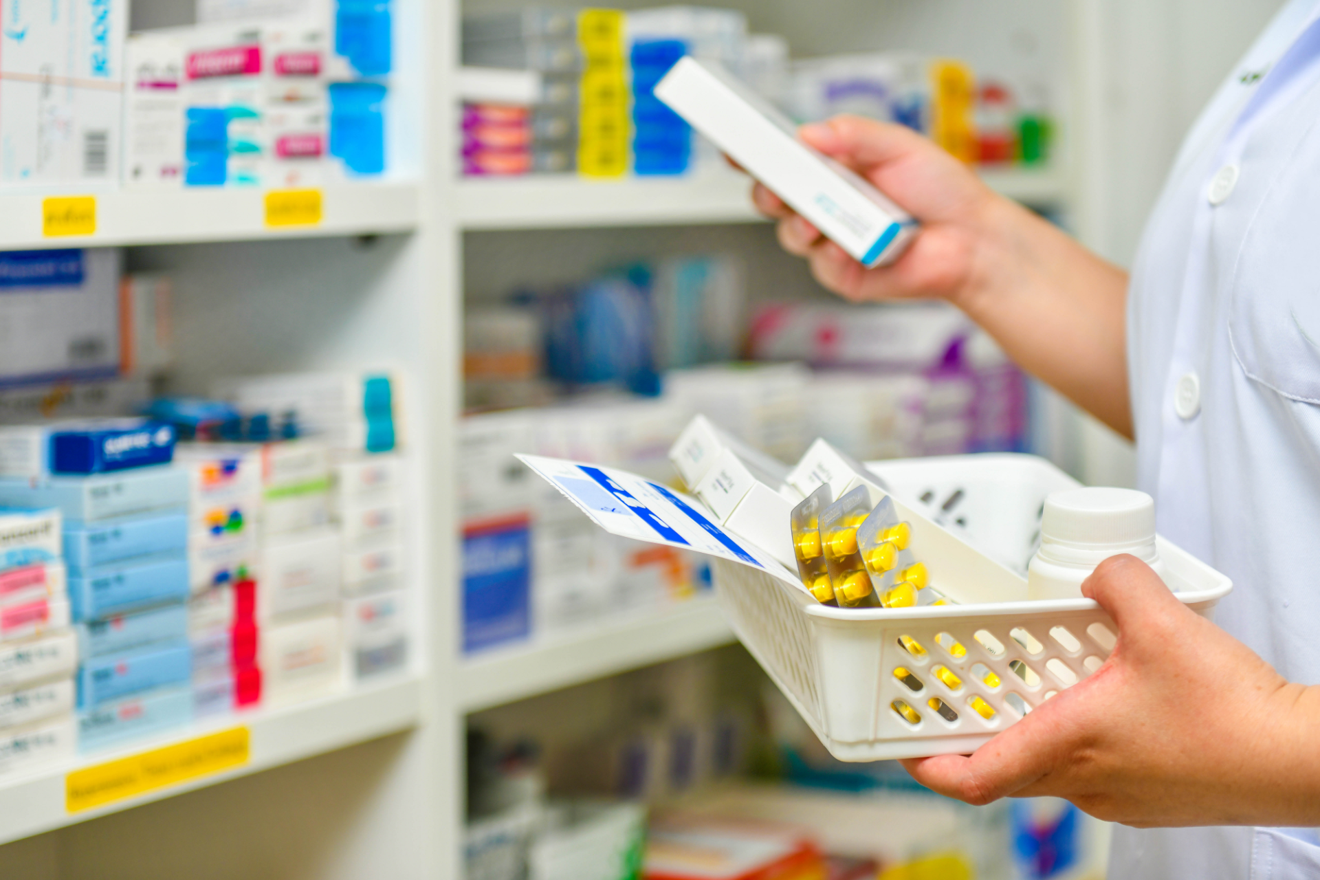 Pharmacist holding medicine boxes and pill tray in a pharmacy aisle