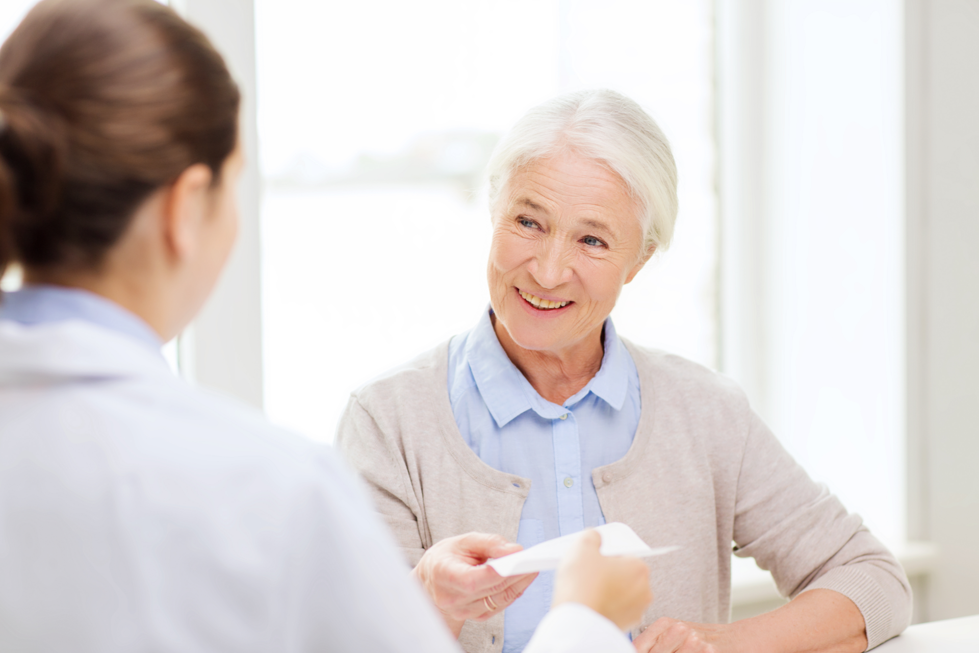 Doctor speaking with smiling patient in a bright clinic, holding a paper form.