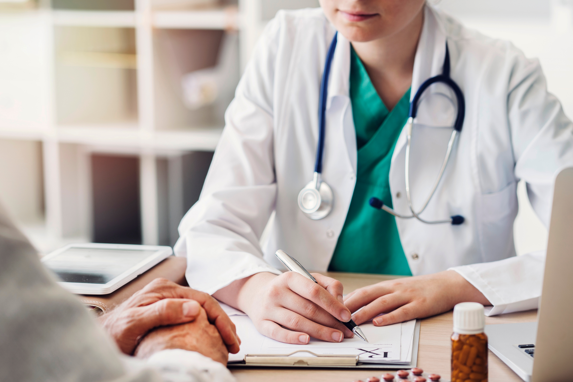 Doctor writing notes beside a patient in a clinic room