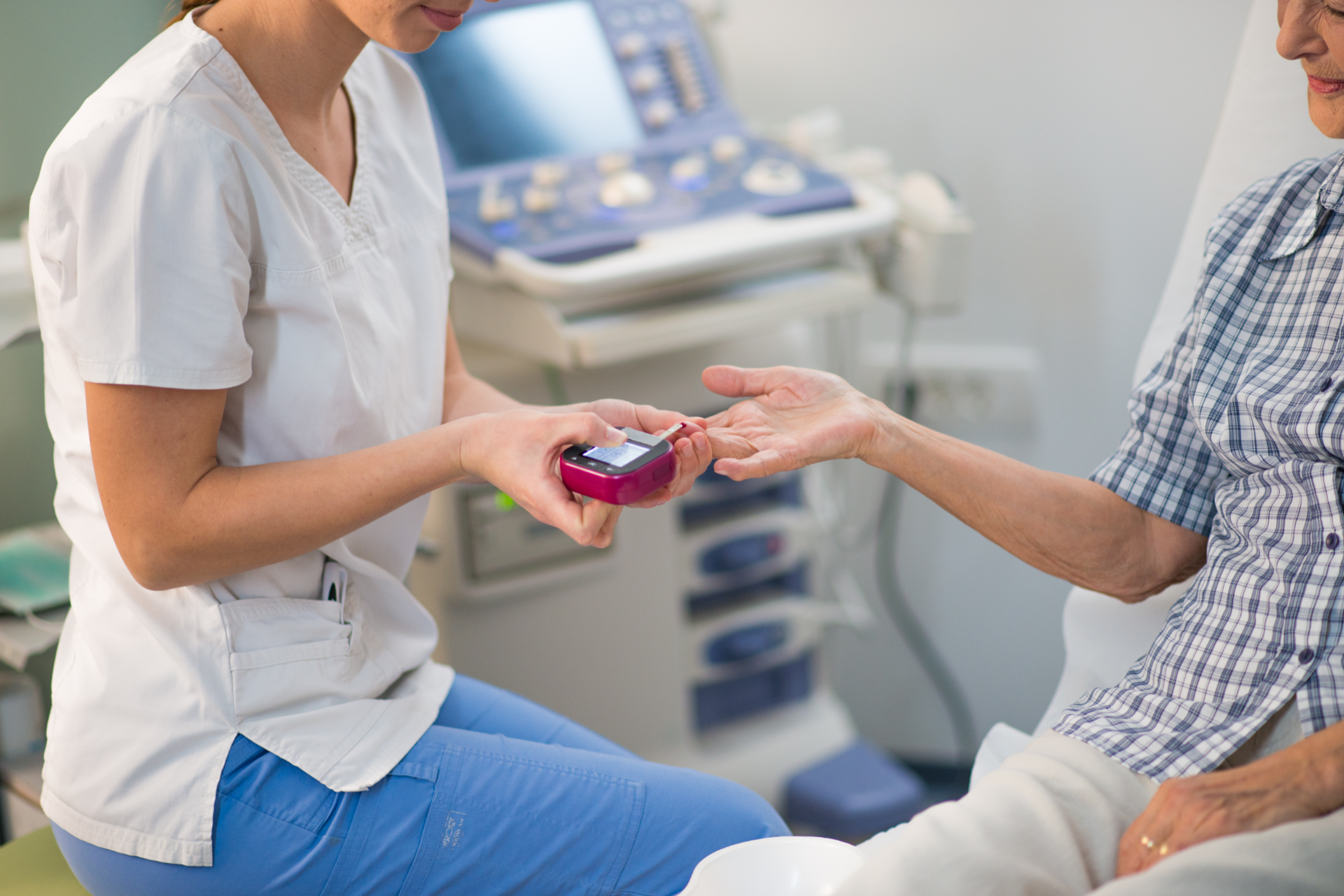 Nurse handing a pink glucometer to a patient in a clinic exam room