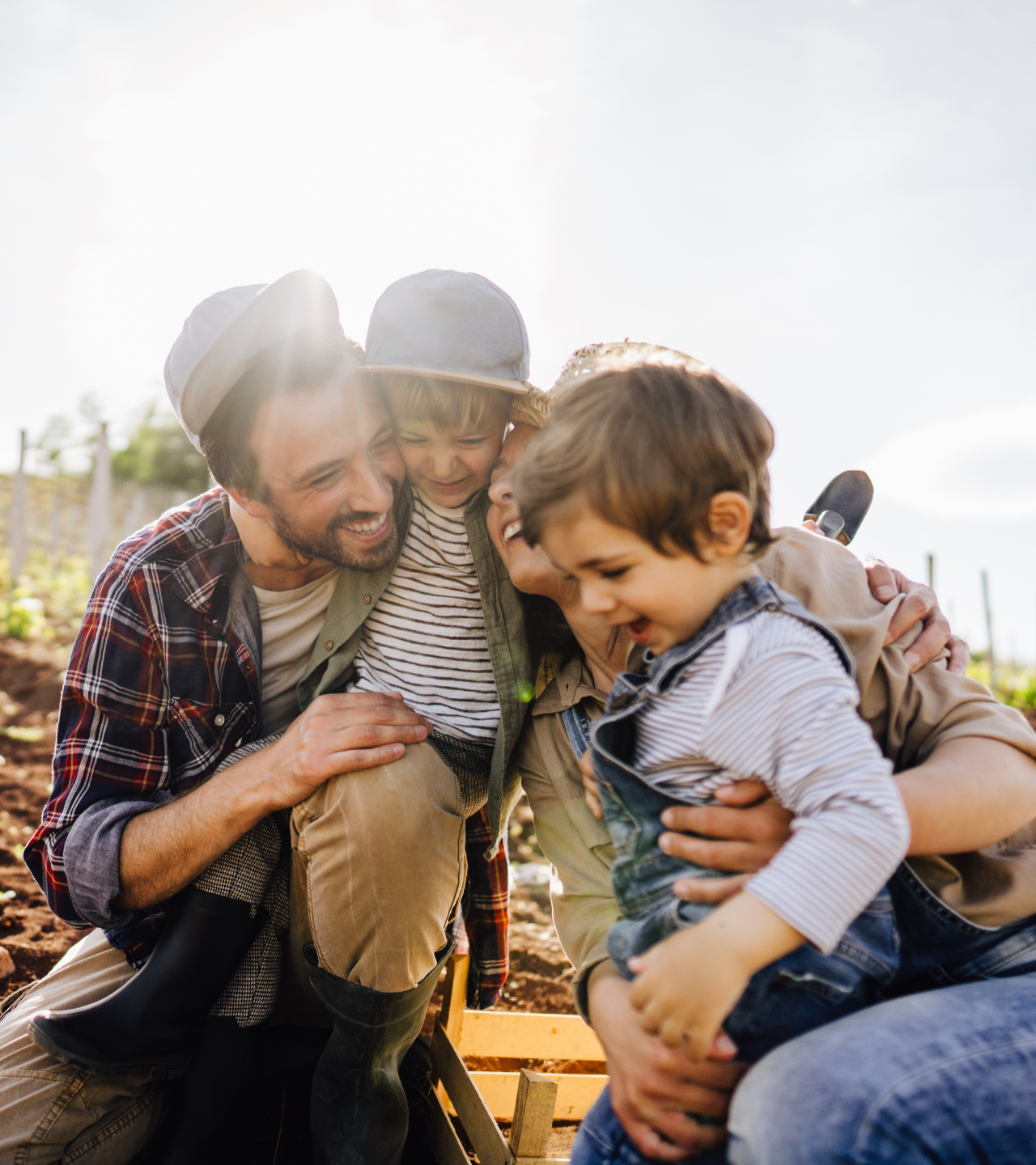 Two adults and two children laughing together outdoors in warm sunlight