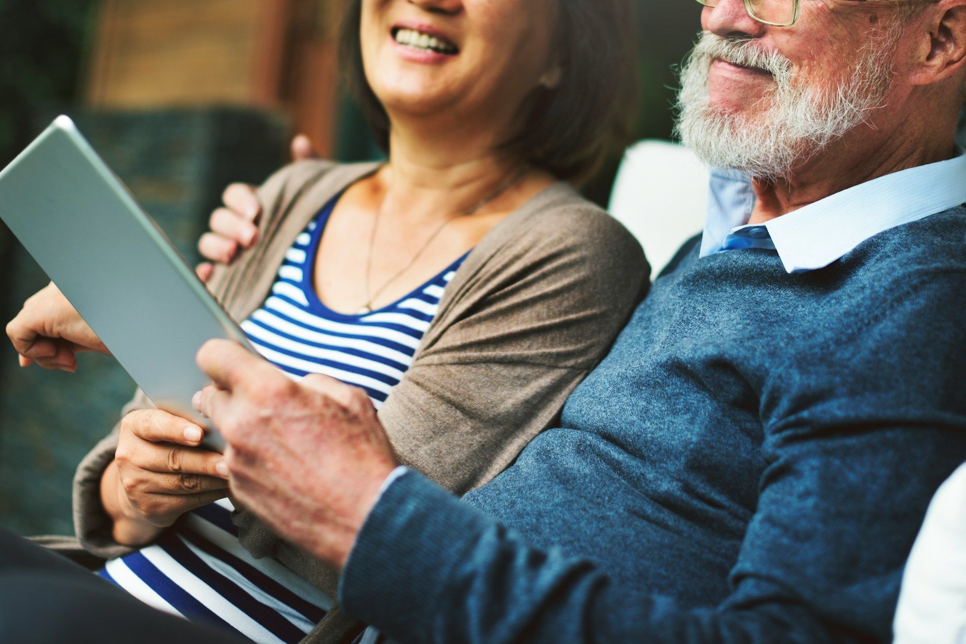 Two people smiling on a couch, looking at a tablet together.
