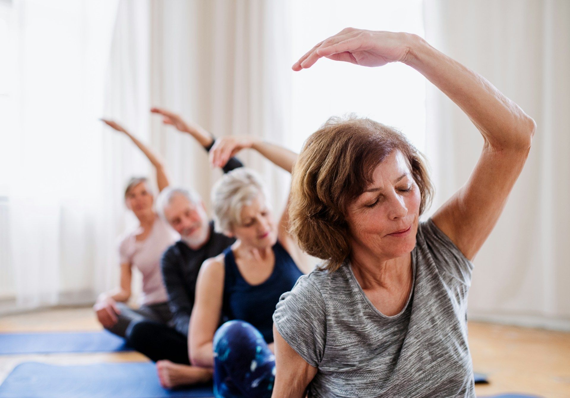 People doing a seated stretching exercise class on blue mats in a bright studio