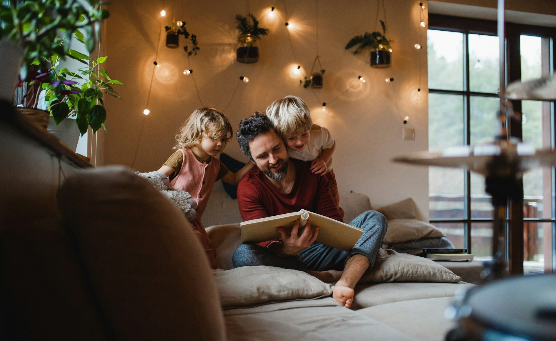 Family reading together on a couch in a cozy, warmly lit living room with string lights.