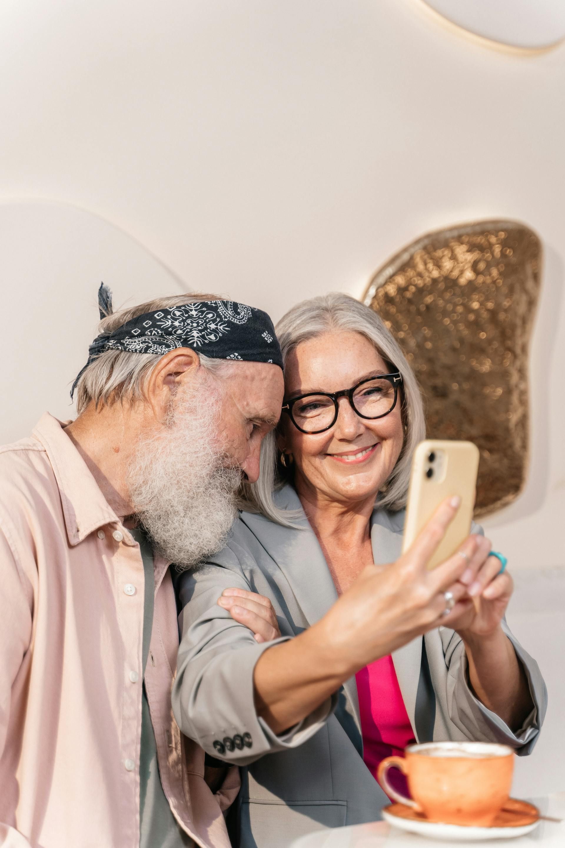 Two people smiling and taking a selfie at a table with a cup of coffee