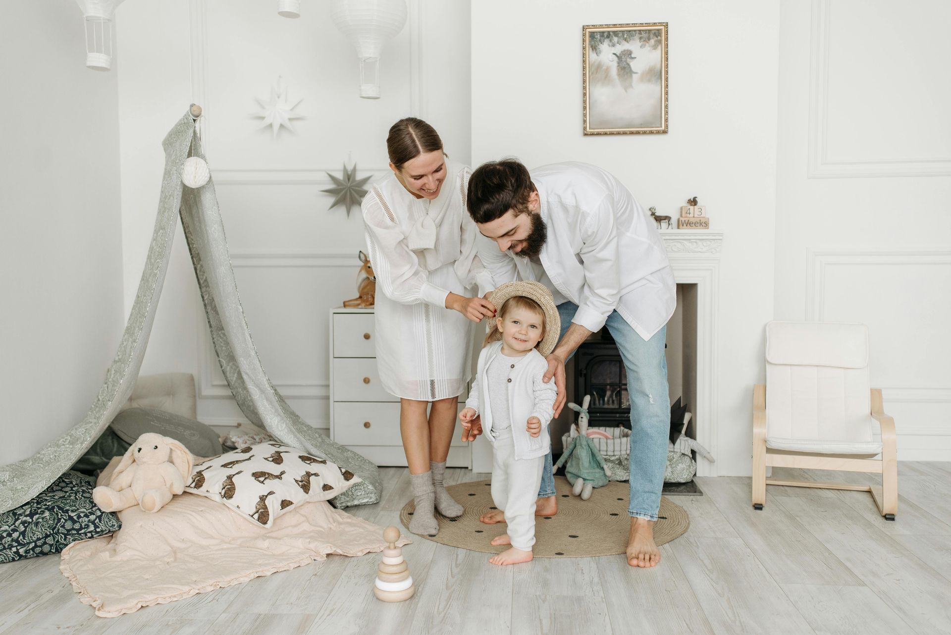 Family playing with a toddler in a bright nursery with a teepee, rocking chair, and toys