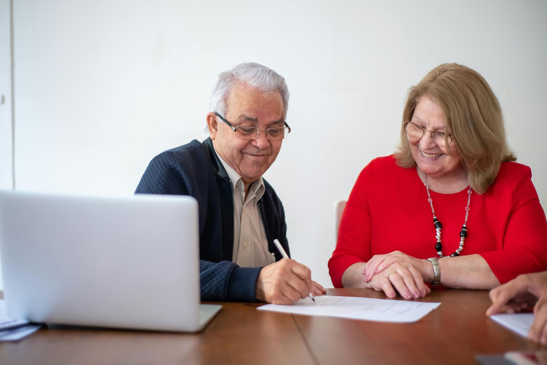 Two people collaborating at a table, reviewing and signing a document beside a laptop.