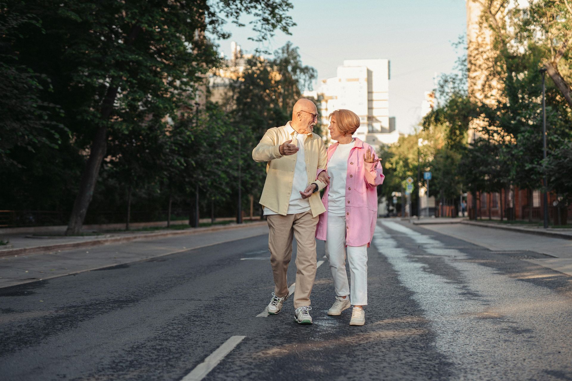 Two people walking together on a tree-lined city street at sunset.