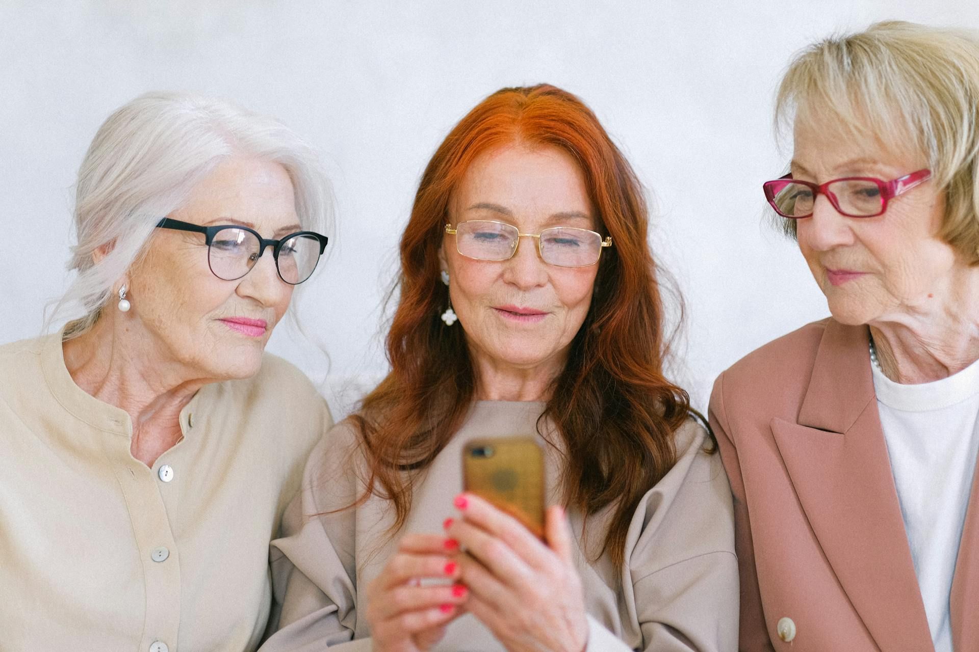 Three women looking at a smartphone together, one holding it, in a bright indoor setting