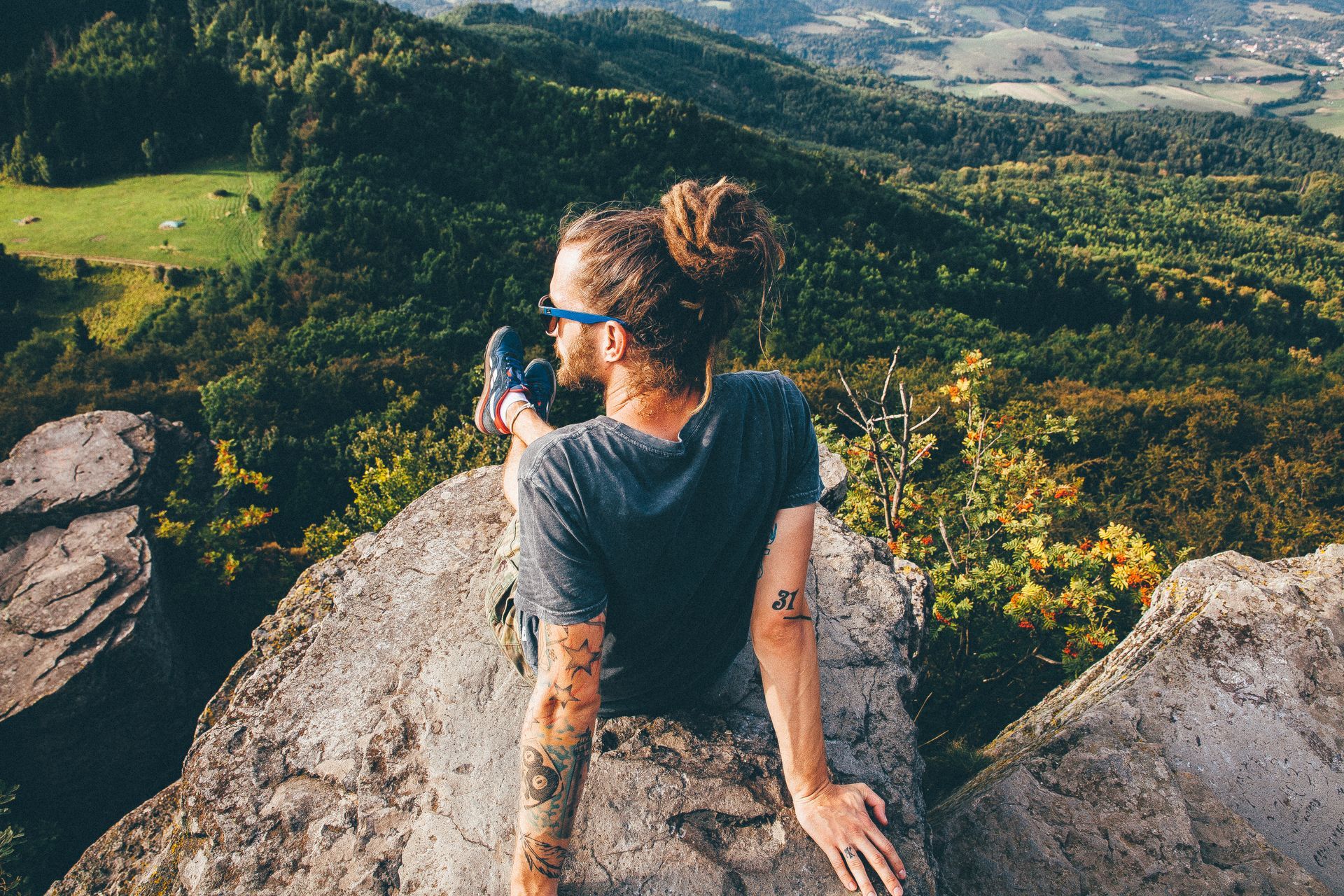 Woman sitting on a rocky overlook, wearing sunglasses and looking over a green mountain valley.