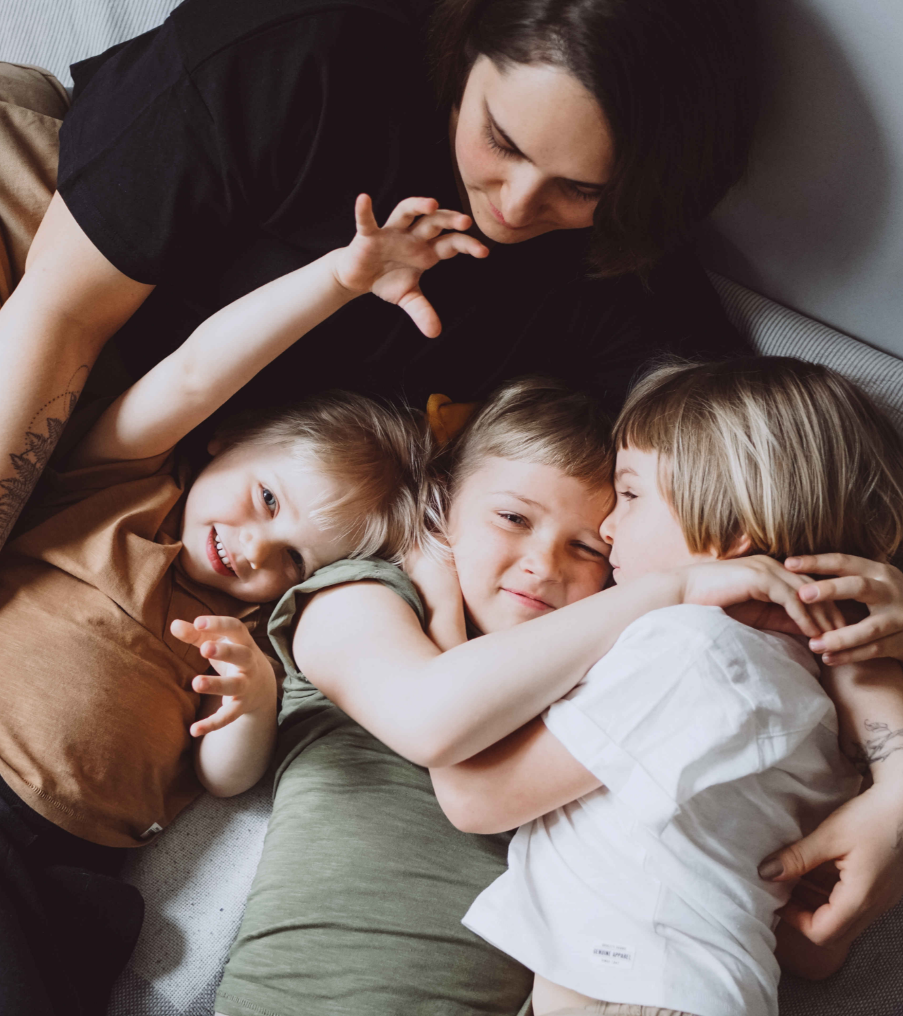 Woman cuddling three children on a bed, smiling and embracing each other.