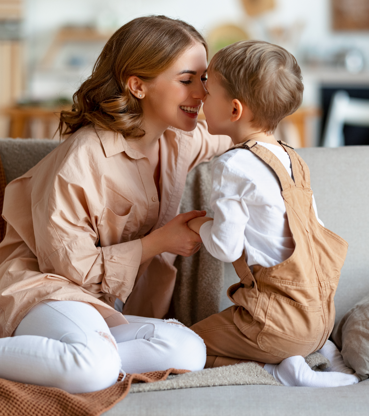 Woman smiling at a child on a couch, touching noses in a cozy living room.