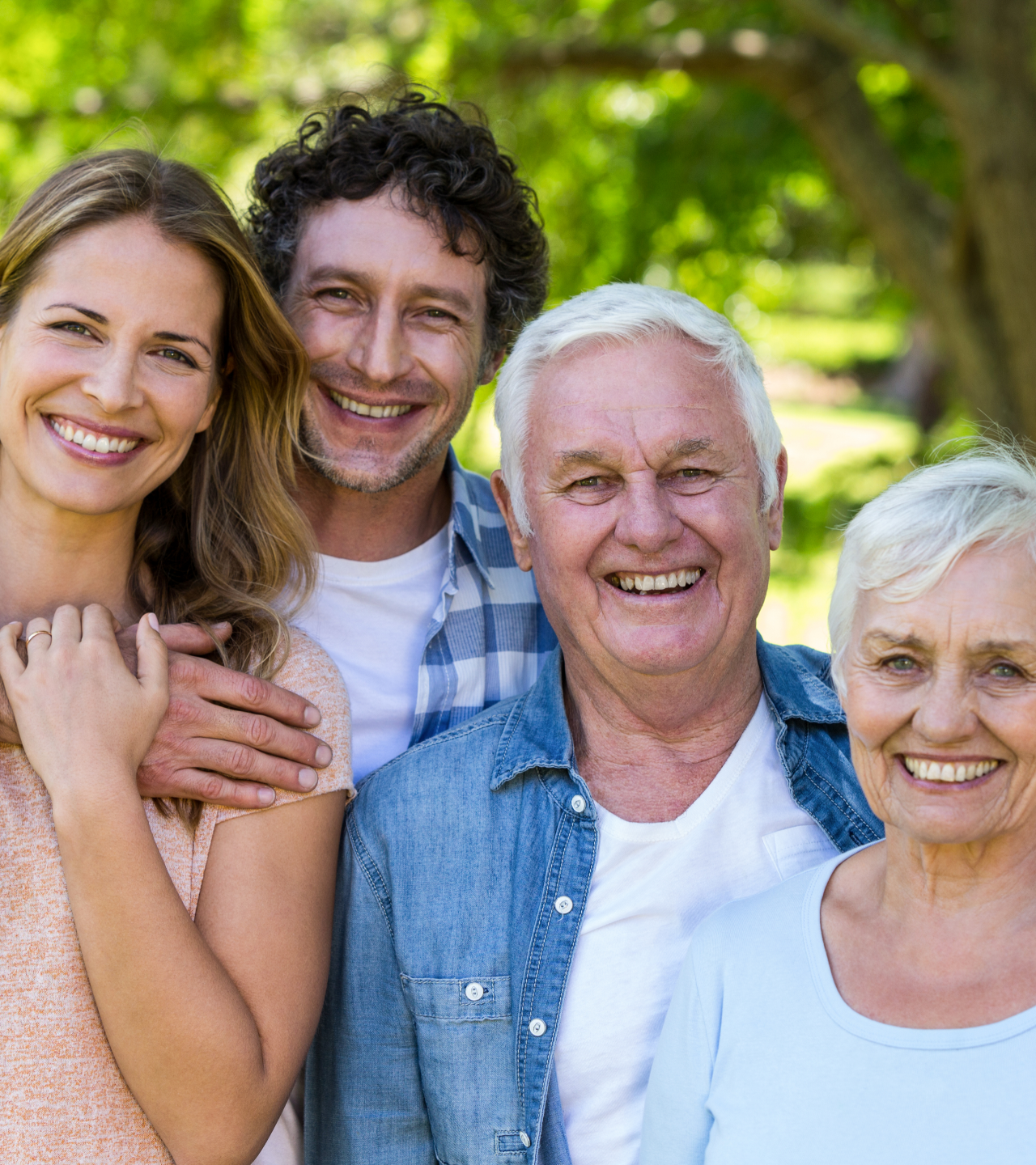 Four smiling people standing close together outdoors in a sunny green park