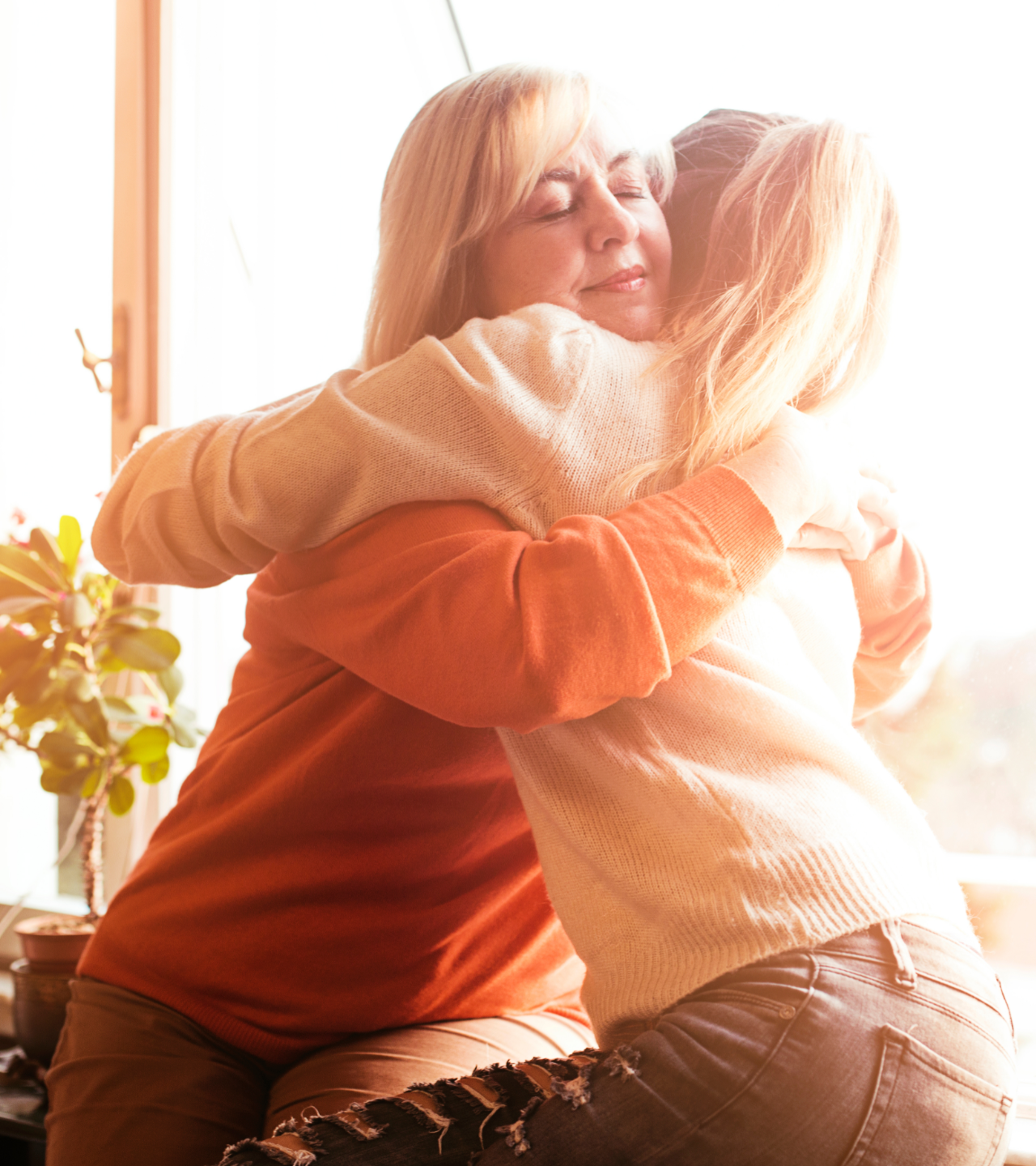 Two people hugging on a sunlit couch near a window