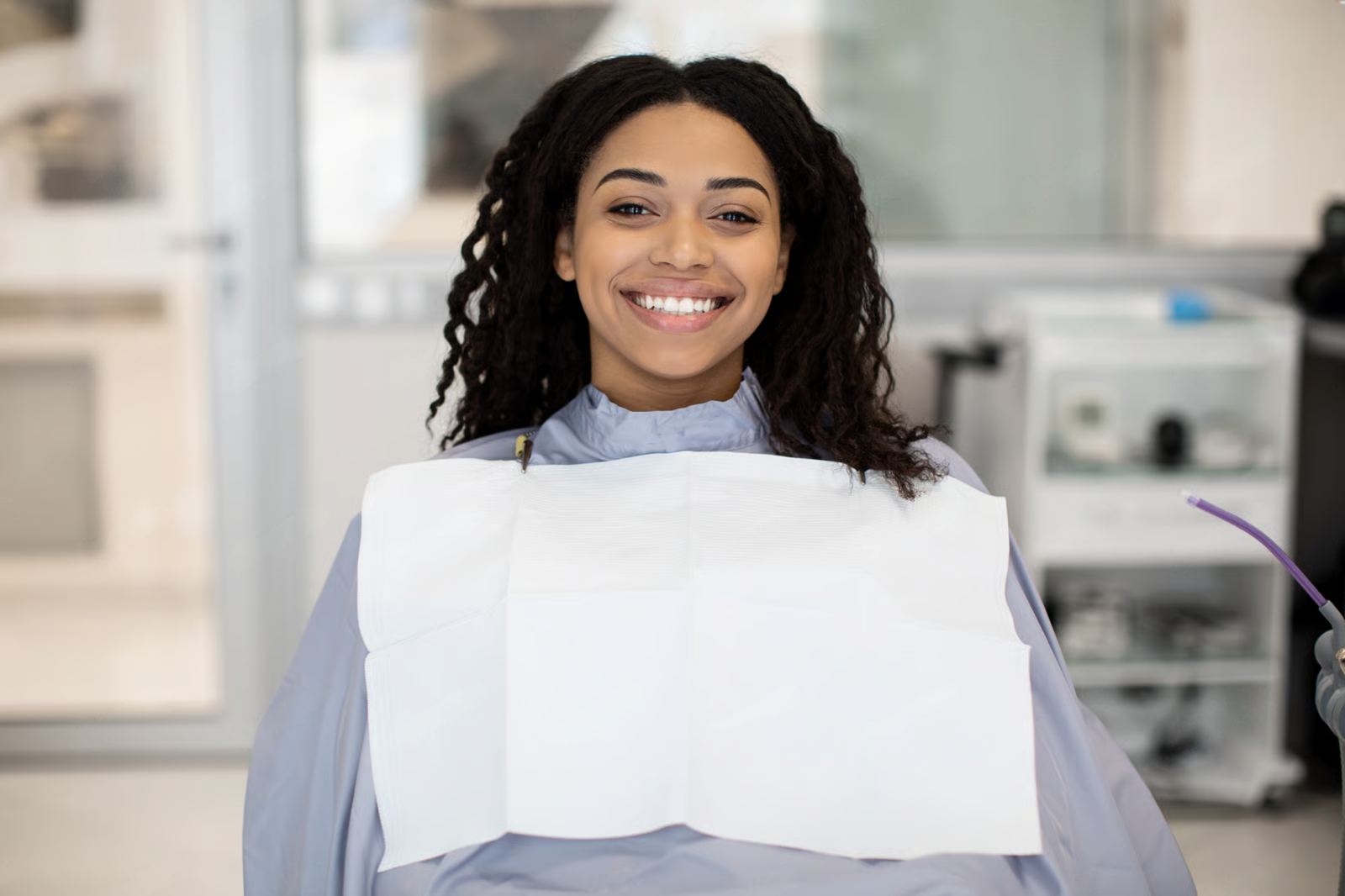 Smiling dental patient wearing a bib and seated in a dentist’s chair