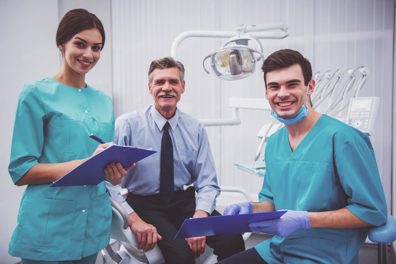 Dentist and two hygienists smiling in a dental clinic, holding clipboards near exam chairs