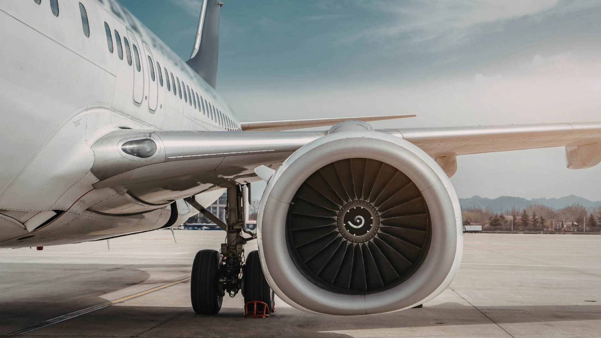 Close-up of a commercial airplane engine and landing gear on the tarmac with mountains in the background