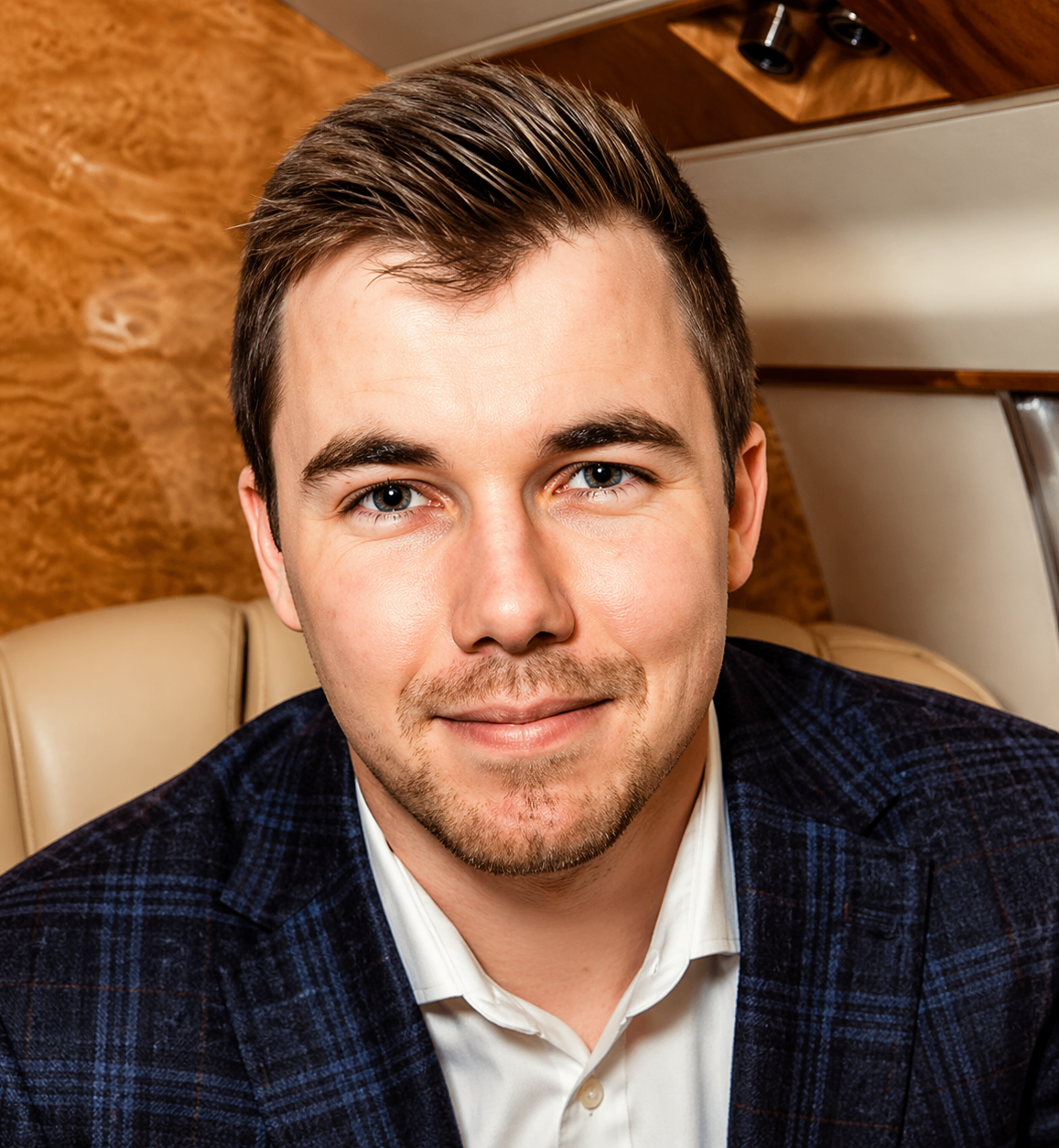 Smiling man in a navy blazer seated in a tan leather seat, with a wood-paneled background
