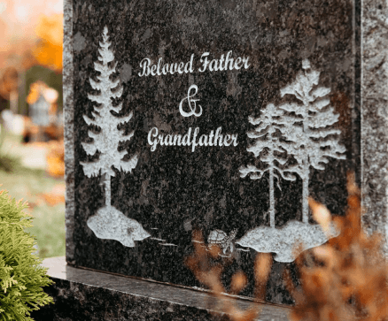 A gravestone for a beloved father and grandfather with trees on it.